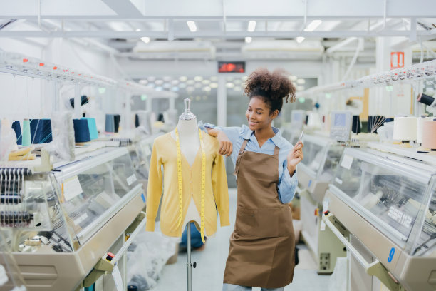 卷发美国女设计师站在纺织业她的周围是一台正在工作的缝纫机，旁边是一个设计衣服的人体模型和一根卷尺。图片下载