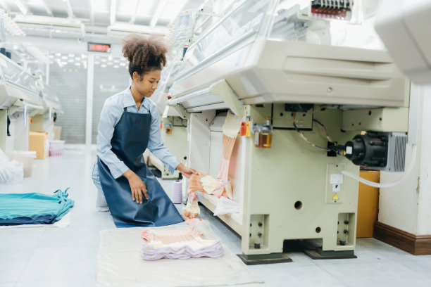美国女设计师是一位女裁缝。在一家大型织造厂，她坐在缝纫机旁检查自己设计的布料。她穿着制服。图片下载