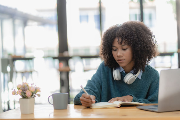 专注于年轻的非洲大学生在客厅用笔记本电脑工作，并使用笔记本电脑在线学习。微笑的女孩观看网络研讨会或远程教育课程图片下载