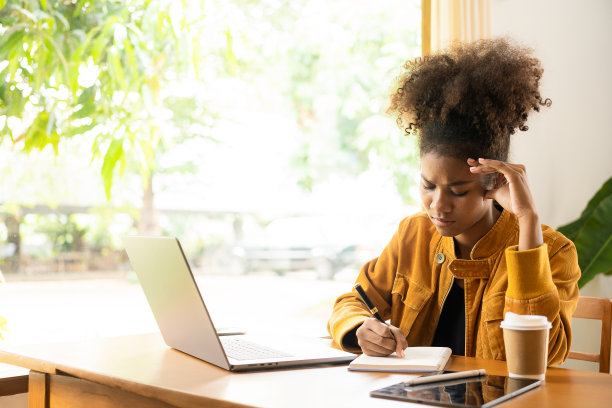 专注于年轻的非洲大学生在客厅用笔记本电脑工作，并使用笔记本电脑在线学习。微笑的女孩观看网络研讨会或远程教育课程图片下载