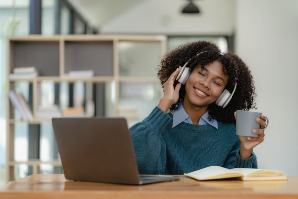 专注于年轻的非洲大学生在客厅用笔记本电脑工作，并使用笔记本电脑在线学习。微笑的女孩观看网络研讨会或远程教育课程图片下载