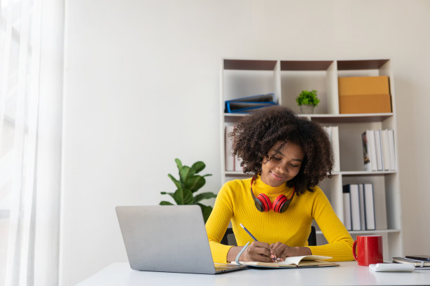 专注于年轻的非洲大学生在客厅用笔记本电脑工作，并使用笔记本电脑在线学习。微笑的女孩观看网络研讨会或远程教育课程图片下载