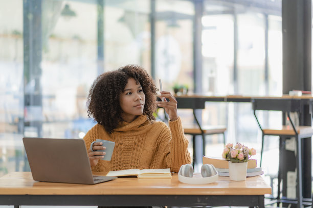 专注于年轻的非洲大学生在客厅用笔记本电脑工作，并使用笔记本电脑在线学习。微笑的女孩观看网络研讨会或远程教育课程图片下载