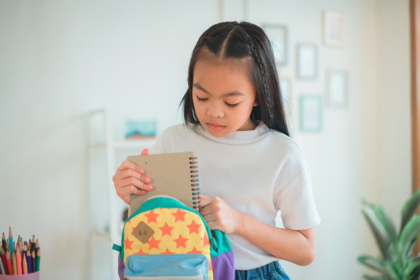 小学生把书和笔记放进书包里。学习用品。回到学校的概念。孩子们准备学习。肖像可爱的小女孩打包背包。图片下载