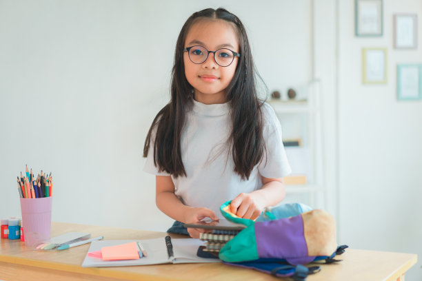 小学生把书和笔记放进书包里。学习用品。回到学校的概念。孩子们准备学习。肖像可爱的小女孩打包背包。图片下载