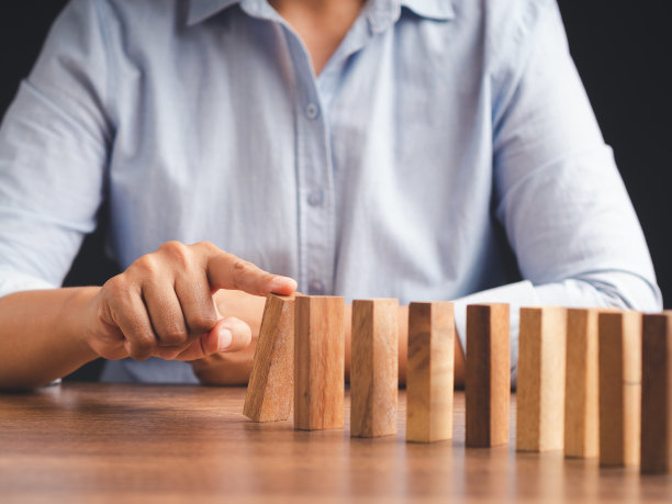 一个商人坐在办公室里推着一排多米诺骨牌上的木块的手。图片下载