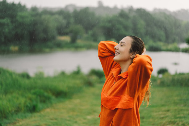 一个穿着橙色毛衣的年轻女孩在夏日的雨中享受的肖像。图片下载