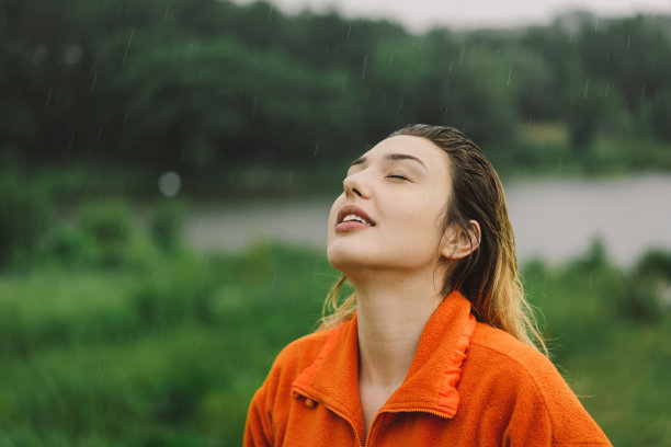 一个穿着橙色毛衣的年轻女孩在夏日的雨中享受的肖像。图片下载