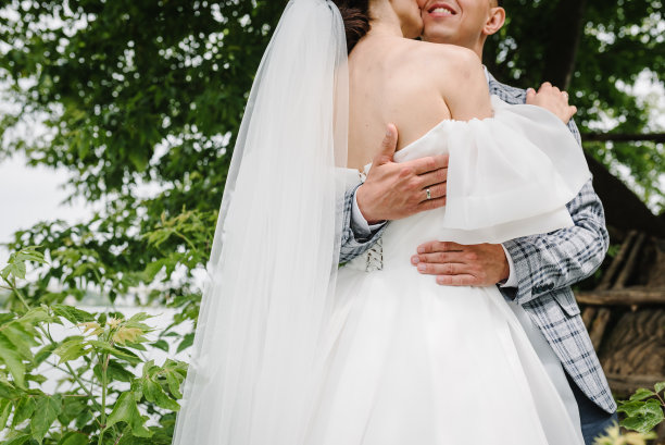 新娘和新郎在自然中亲吻和拥抱。新婚夫妇站在湖边的一棵大树旁。一个乡村爱情故事。新婚快乐。在户外结婚。特写镜头。图片下载