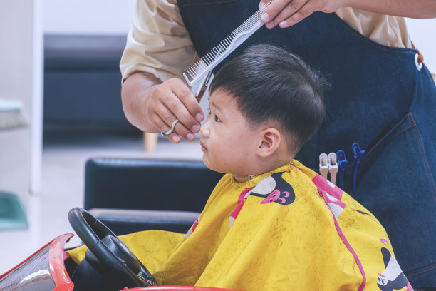 2岁的亚洲男孩坐在玩具车形状的高脚椅上，在儿童理发店理发图片下载
