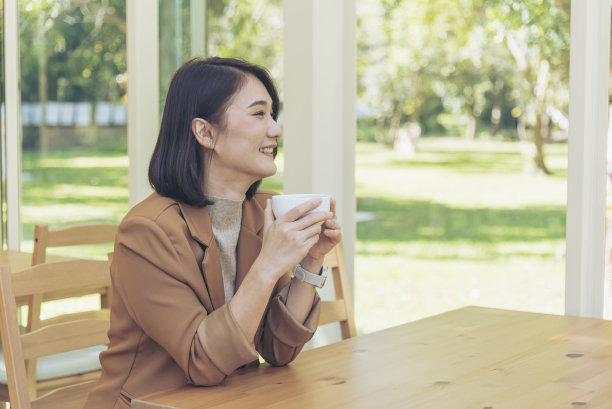 美女拿着新鲜的杯子在咖啡店喝黑咖啡。咖啡爱好者。亚洲妇女在绿花园咖啡馆用手捧杯喝黑咖啡。年轻女子笑着脸爱喝咖啡图片下载
