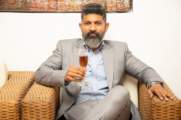 留胡子的印度商人坐在沙发上，手里拿着一杯酒，企业男性庆祝公司的成功。图片下载