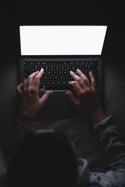 一个女人晚上在沙发上用笔记本电脑工作。晚上在笔记本电脑上工作。上网。雇佣女性。白色的屏幕。股票的照片。图片下载