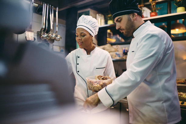 非裔美国厨师和她的男同事在餐厅厨房准备食物。图片下载