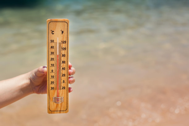 海滩背景下手持温度计，显示高温，炎热天气和气候概念图片下载