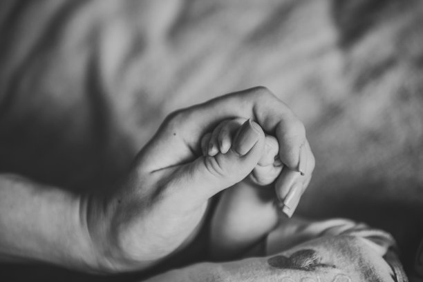 宝宝的手。年轻的母亲握着孩子的手。可爱的小婴儿躺在家里的床上。妈妈握住儿子的手指。特写镜头。新生女孩或男孩的小手握在手里。女儿睡觉。黑白照片。图片下载