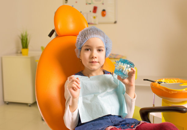 一个小女孩坐在牙科诊所的椅子上，手里拿着一个下巴模型。牙科保健，口腔卫生。图片下载