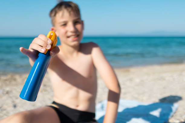 男孩正在阳光明媚的海滩上涂抹防晒霜图片下载