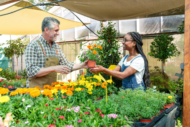 在郁郁葱葱的花店里，一位微笑的高级苗圃工作人员向非洲顾客赠送盆栽植物，五彩缤纷。图片下载