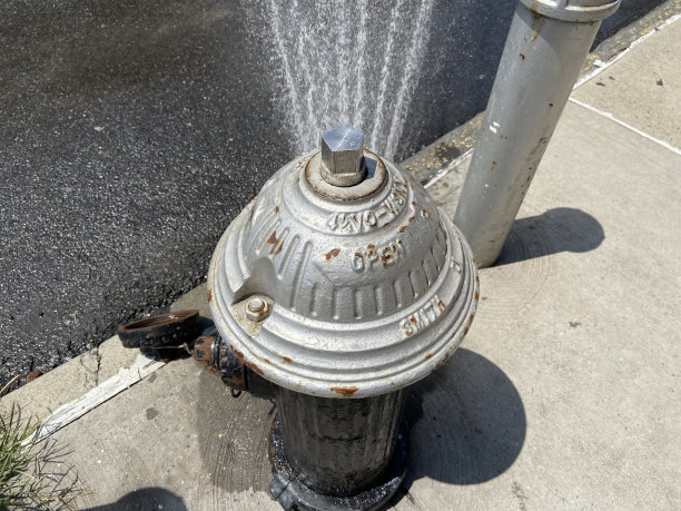 在纽约炎热的夏日，一个银色的消防栓顶部向街道喷水的特写图片下载