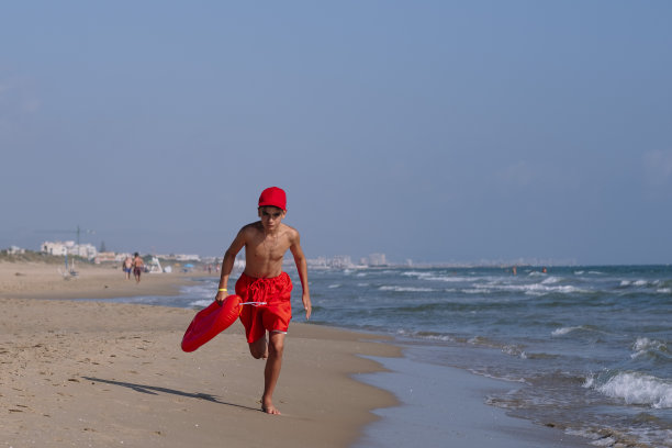 救生员男孩带着救生筏在沙滩上奔跑图片下载