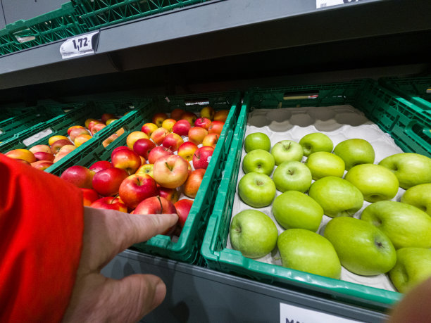 一个男人的手指着陈列出售的红苹果。图片下载