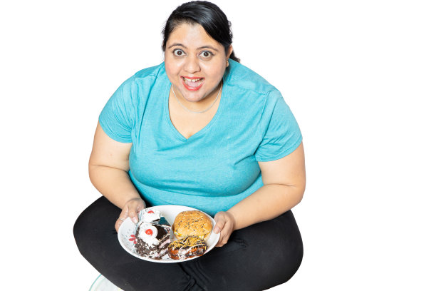 超重的印度妇女坐在盘子里，盘子里装满了不健康的食物，比如蛋糕、甜甜圈和汉堡，在白色的背景上孤立起来图片下载