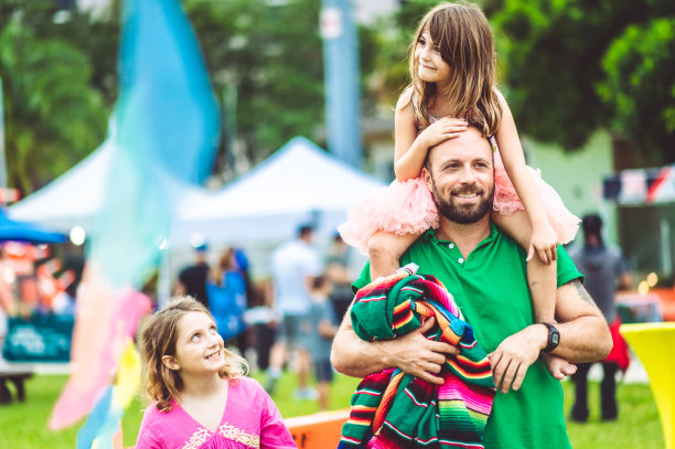 父亲带着两个孩子在户外的夏日狂欢节集市或游乐园，阖家欢乐图片下载