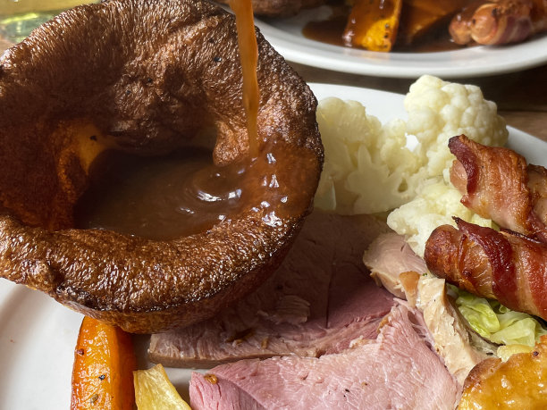 全画幅图片，肉汁倒在白色盘子里，盘子里装着星期天的烤晚餐、约克郡布丁、胡萝卜、防风草、烤土豆、卷心菜、花椰菜、裹着毯子的猪、烤火腿图片下载