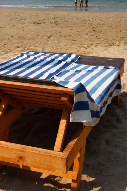 两个人的特写图像，木质蒸笼躺椅在沙滩上擦拭干净的垫子，蓝色和白色的条纹毛巾，沙滩，低潮的大海，破碎的海浪，重点在前景图片下载