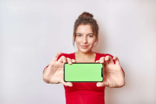 漂亮女孩拿着绿色屏幕的智能手机。图片下载