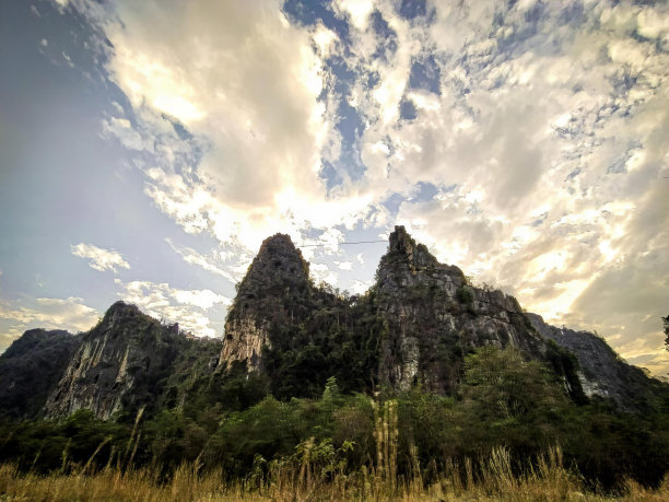 有一架飞机飞过一座山的照片，有一架飞机飞过一座山，天空多云。图片下载