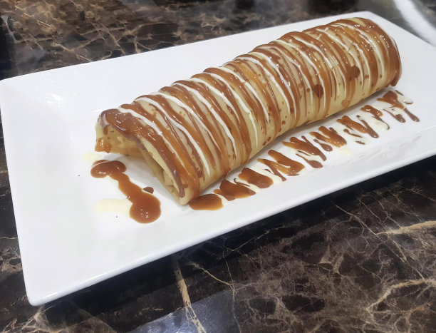 一张白色盘子上有焦糖酱的糕点的照片，盘子上有一个长长的焦糖酱糕点。图片下载