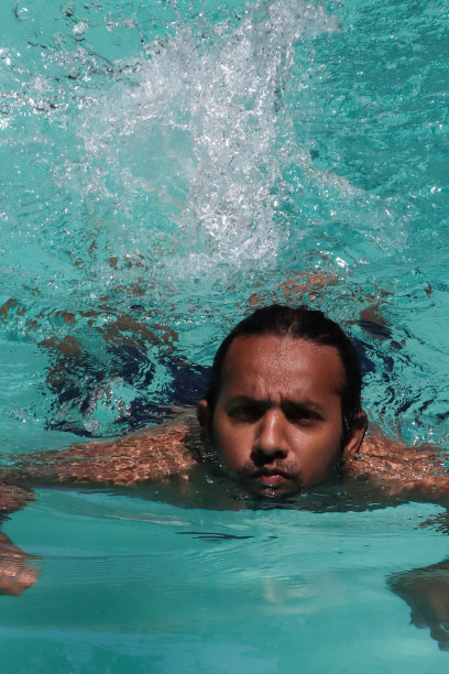 印度男子在清澈的水中做蛙泳的特写，室外，游泳池，绿松石蓝色马赛克瓷砖被波纹水扭曲，游泳和飞溅，波涛汹涌的水面反射，重点在前景图片下载
