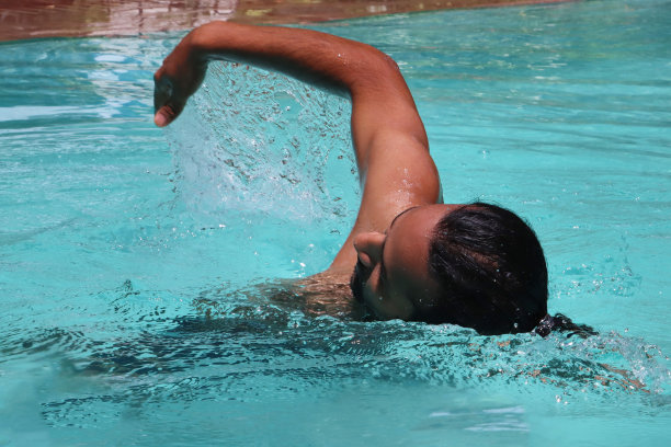 全画幅印度男子在清澈的水中做前爬，室外，游泳池，绿松石蓝色马赛克瓷砖被波纹水扭曲，游泳和飞溅，波涛起伏的水面反射，重点放在前景图片下载