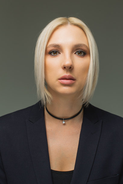 演播室里，灰色背景下身穿黑色西装的金发女商人。肖像图片下载