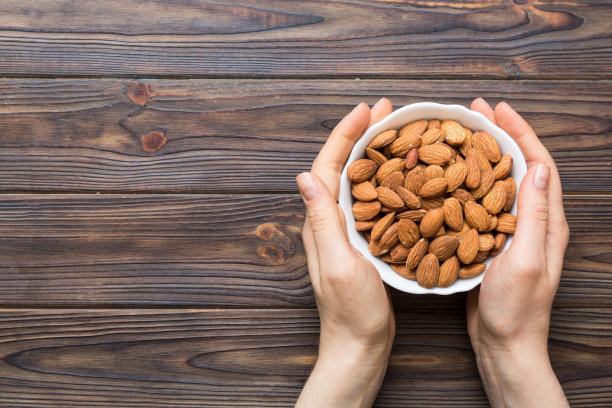 女人手里拿着一个装着杏仁的木碗。健康食品和零食。素食者吃不同的坚果图片下载