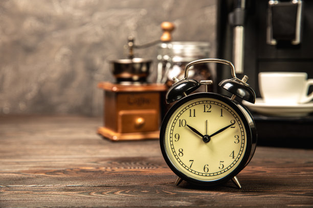 闹钟和一杯早上的咖啡，咖啡机的背景是厨房内部。桌上有一杯咖啡，早上有个闹钟。早上好，概念。醒醒吧!图片下载