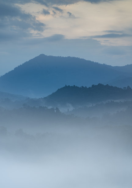 这是一幅宁静的图像，一个雾蒙蒙的山谷，层层叠叠的小山逐渐消失在远处，周围是宁静的气氛和微妙的橙色和蓝色图片下载