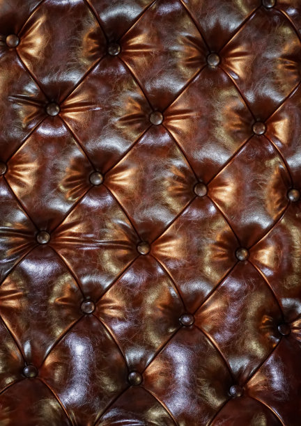 真正豪华的一个优雅的复古切斯特菲尔德图案棕色皮革沙发，座位，坐垫，软垫家具在复古风格深钮扣图案，棕色皮革衬垫背景。特写镜头图片下载