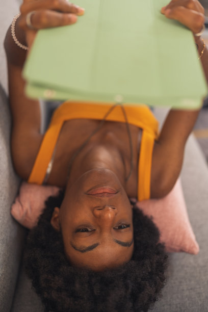 年轻的黑人女性躺在床上玩她的电子平板电脑图片下载