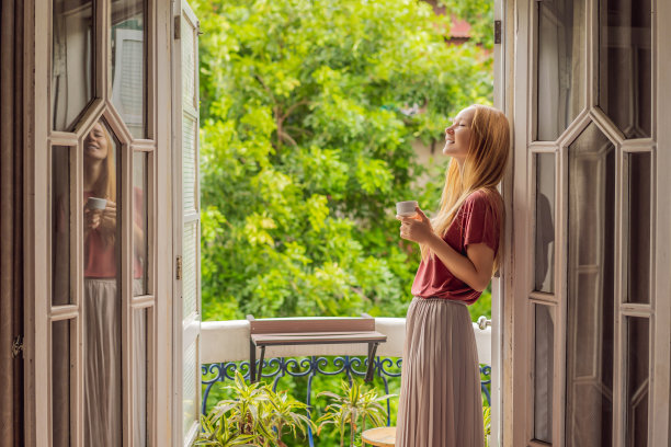 一个姜黄色头发的女人站在传统风格的阳台上享受她的早晨咖啡。欧洲或亚洲酒店里的一名妇女，旅游业正从大流行中复苏。由于接种疫苗，旅游业已经恢复。该女子在酒店被隔离了14天。图片下载