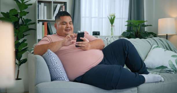 胖乎乎的男人用智能手机在客厅的沙发上放松图片下载