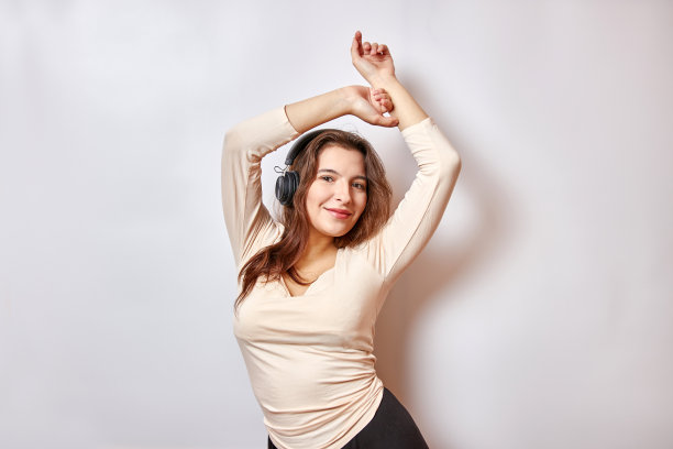 美丽的女孩带着快乐和微笑听着耳机上的音乐。图片下载