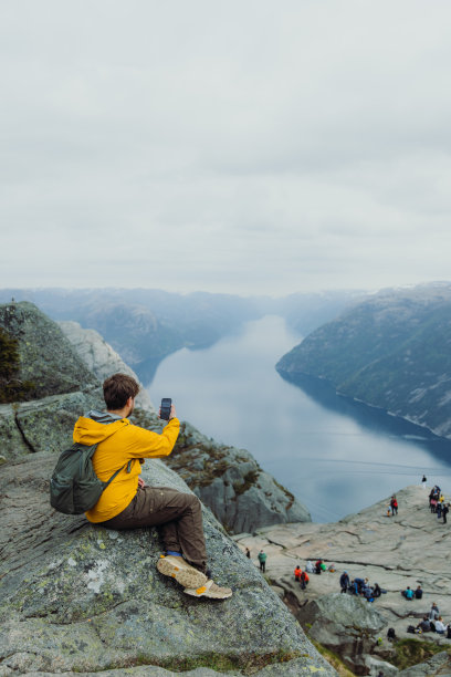 一名男子在山顶上用智能手机观看挪威布道石的美景图片下载