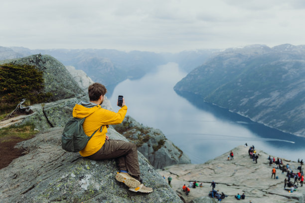一名男子在山顶上用智能手机观看挪威布道石的美景图片下载