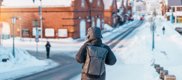 在函馆参观的男游客，穿着毛衣的游客在冬天的雪中游览金森红砖仓库。它是日本北海道的地标和著名景点。旅游度假概念图片下载