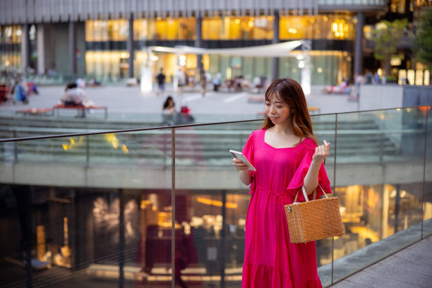 穿着粉色裙子的女人走在城市里，手里拿着智能手机图片下载