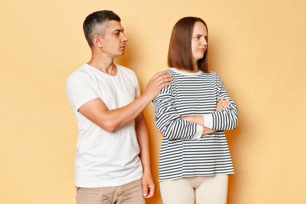 我们能试着和解吗?年轻的男友丈夫抚摸着被冒犯的女友妻子的肩膀，提议讲和，争吵后和解，隔着米色的背景。图片下载