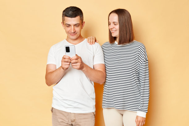 微笑积极的年轻夫妇，朋友，男人，女人，穿着休闲服，用手机上网，一起孤立的米色背景图片下载